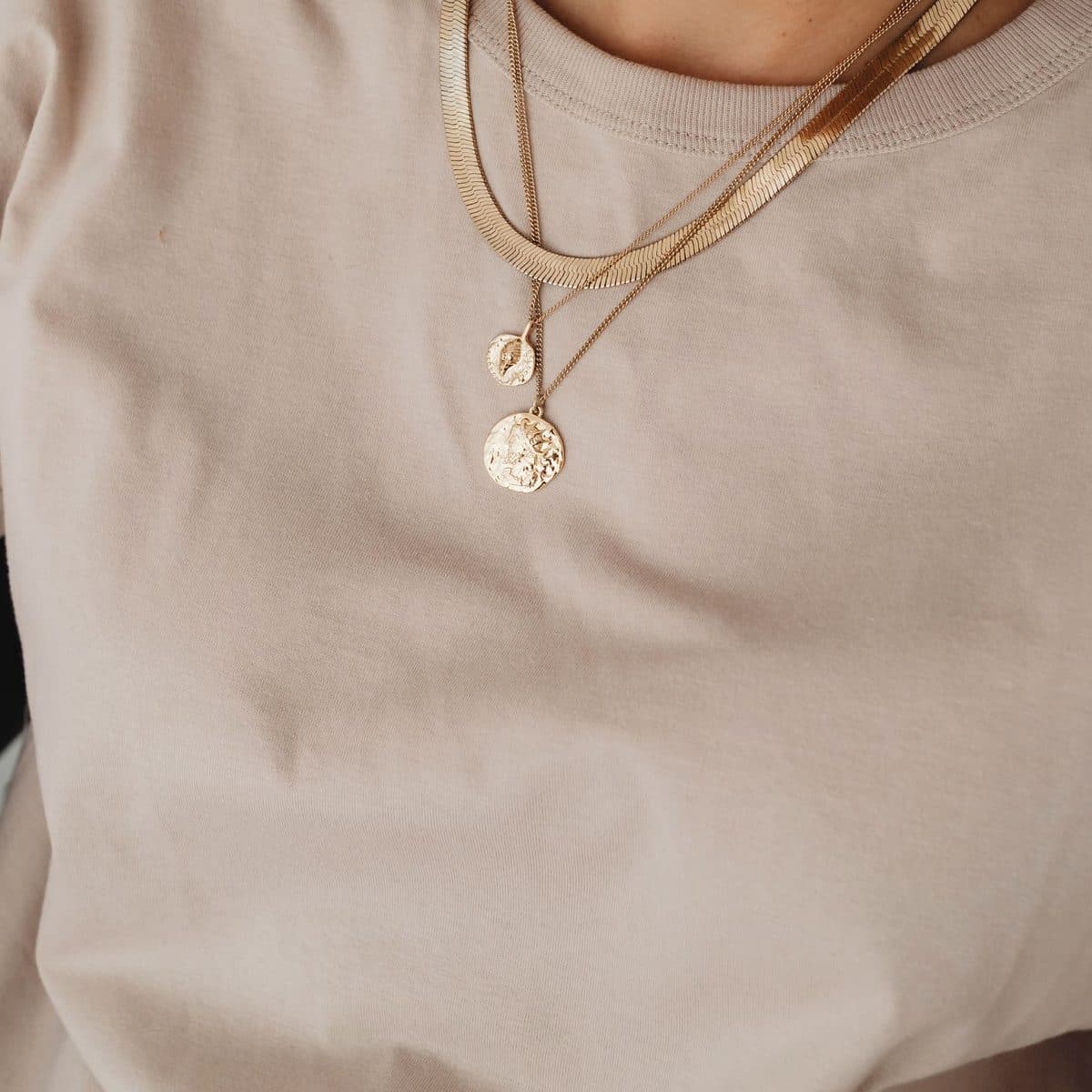 Collares finos con medalla sobre una polera beige