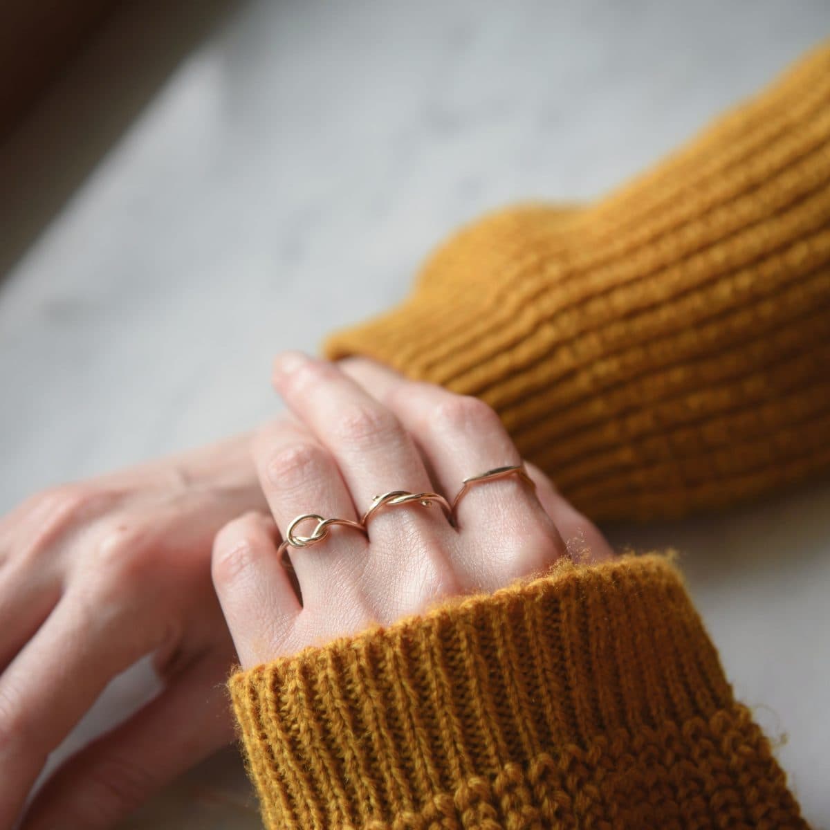 Mano con anillos finos apilados y suéter mostaza